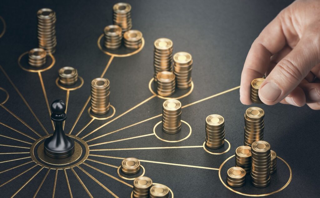 a black pawn chess piece surrounded by several piles of gold coins. A hand is placing another set of coins on top of one of the piles